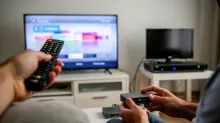 Dos personas sostienen mandos a distancia frente a televisores encendidos en una sala