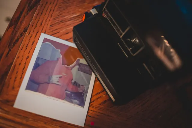 Cámara instantánea junto a un iPhone con fotografías de formato cuadrado sobre una mesa