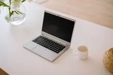 Portátil abierto sobre una mesa junto a una taza y flores