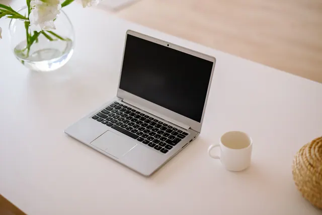 Portátil abierto sobre una mesa junto a una taza y flores
