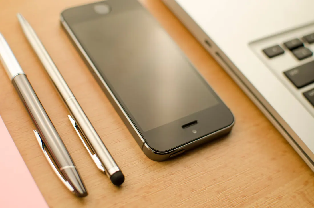 Un teléfono móvil, bolígrafos y un ordenador sobre una mesa