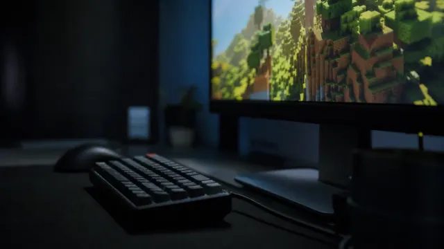 Teclado y ratón sobre escritorio frente a monitor que muestra un paisaje montañoso