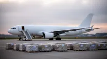 Avión de carga blanco estacionado en pista con palés cubiertos de plástico en primer plano y escalerilla de acceso