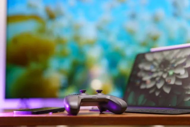 Mando de videoconsola sobre una mesa junto a un portátil y una pantalla