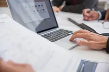 Manos sobre un portátil y documentos durante una reunión de trabajo