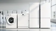 Electrodomésticos de cocina blancos alineados: lavadora, lavavajillas y frigoríficos en interior luminoso