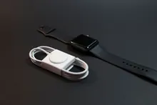 Un reloj Apple Watch junto a su cable de carga sobre fondo negro