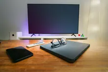 Unas gafas sobre un portátil junto a un móvil, con un televisor al fondo