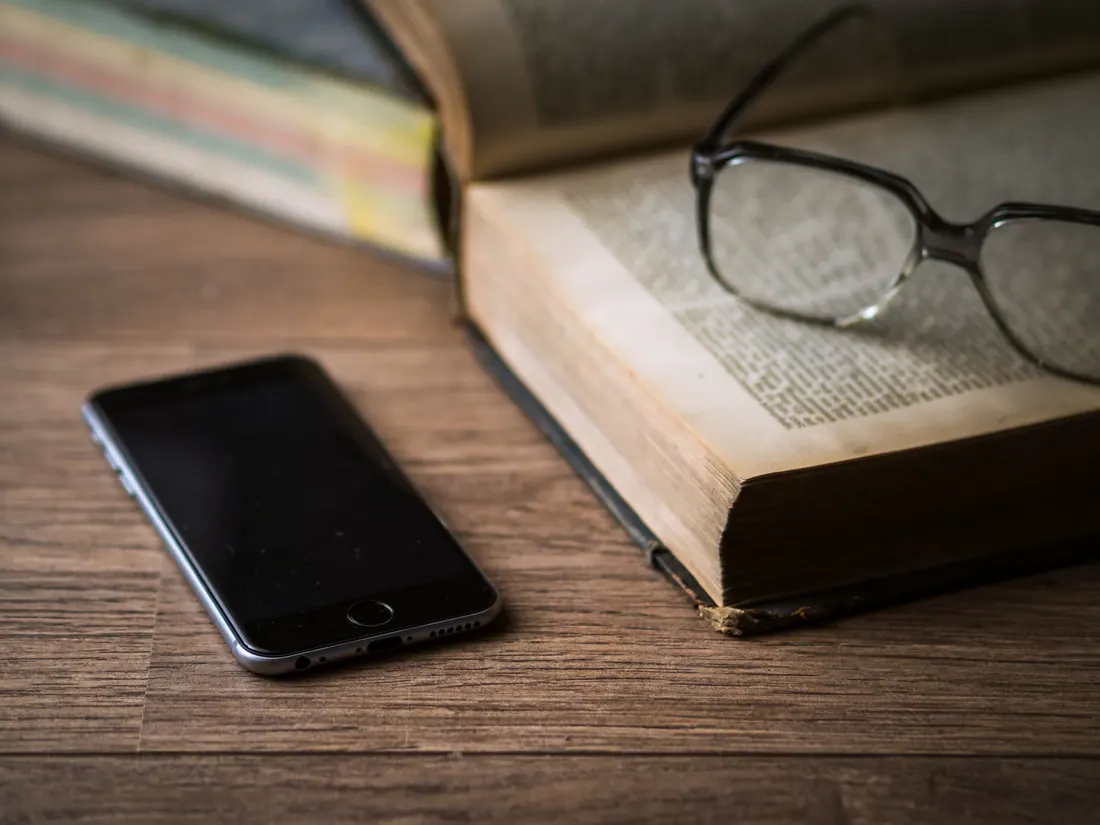 Un teléfono móvil, gafas y libros sobre una mesa de madera