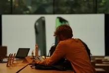 Una persona de espaldas revisa un móvil en una mesa de trabajo con portátiles