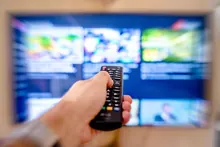 Una mano sostiene un mando a distancia frente a un televisor encendido