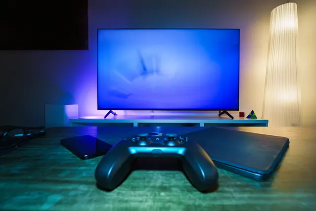 Mando de videoconsola sobre una mesa frente a un televisor encendido