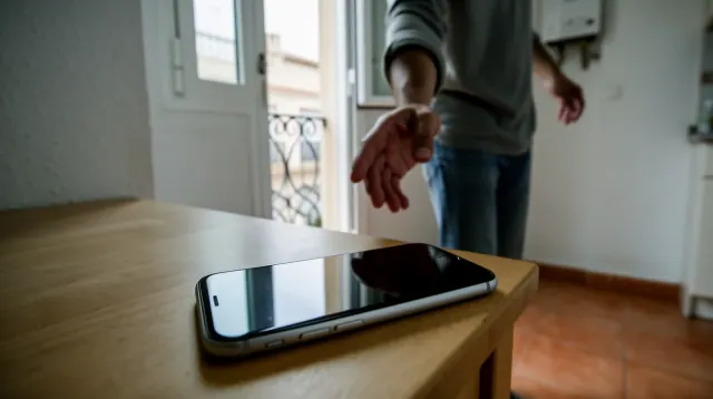 Teléfono móvil sobre mesa de madera con persona entrando por puerta al fondo