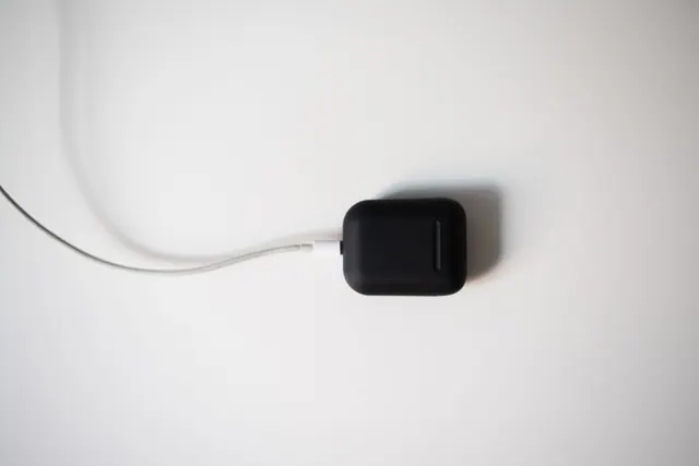 Un estuche de auriculares inalámbricos negro cargándose con un cable sobre una superficie blanca