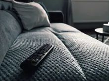 Mando a distancia sobre un sofá frente a un televisor apagado en un salón