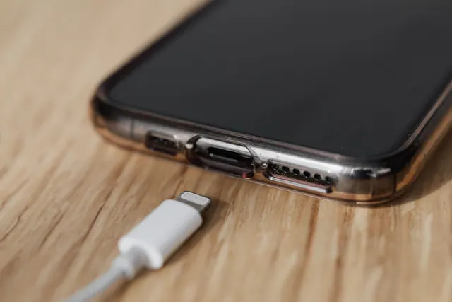 Un iPhone con funda sobre una mesa de madera junto a su cable de carga