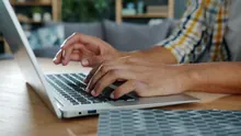 Manos escribiendo en el teclado de un portátil sobre una mesa de madera