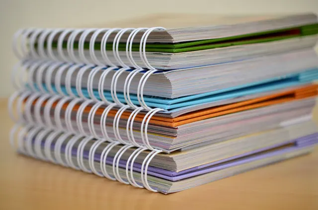 Pila de cuadernos de espiral con tapas de colores verde, azul, naranja y púrpura apilados sobre una superficie