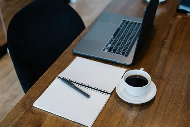 Escritorio de madera con portátil, cuaderno y taza de café
