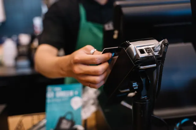 Mostrador de cafetería con taza y terminal de pago contactless sobre madera