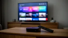 Decodificador y mando a distancia sobre una mesa de madera frente a un televisor