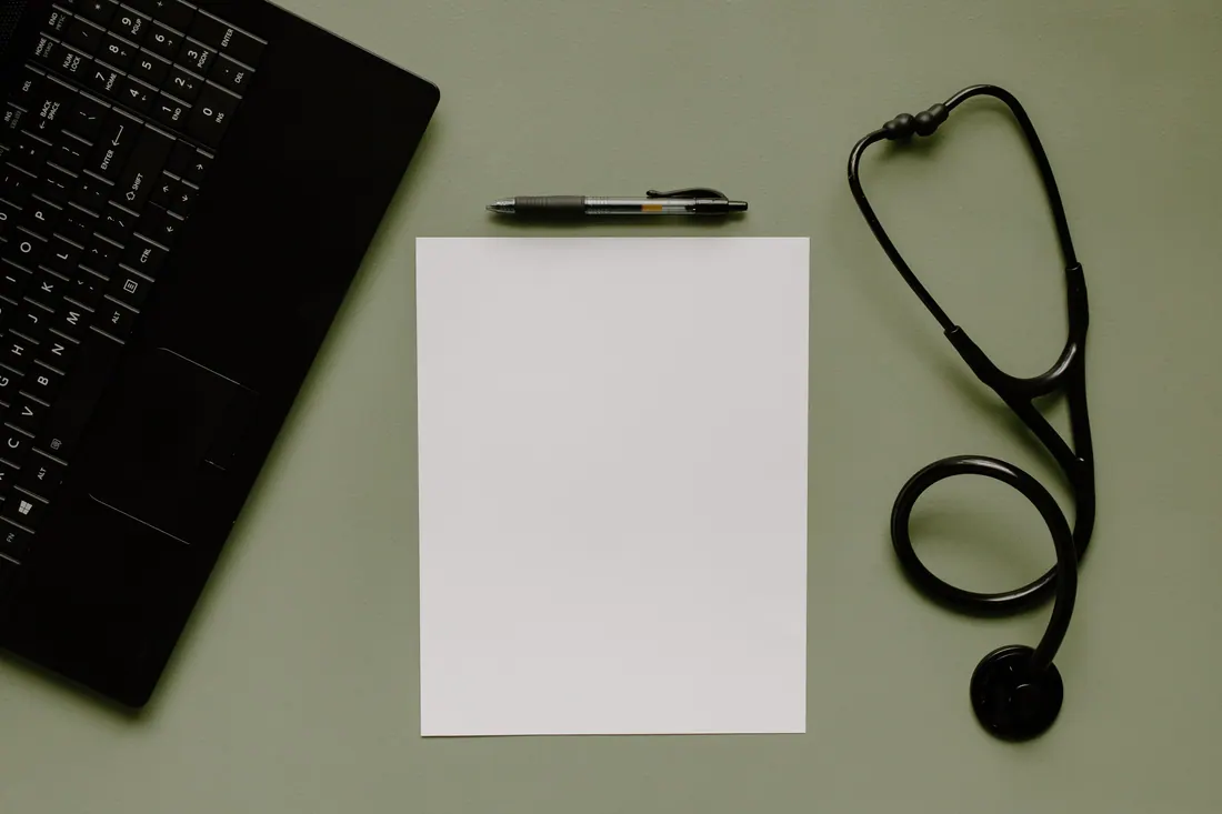 Un teclado, un bolígrafo, un folio en blanco y un estetoscopio sobre una mesa