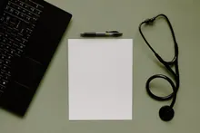 Un teclado, un bolígrafo, un folio en blanco y un estetoscopio sobre una mesa