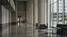 Vestíbulo moderno de edificio con columnas, suelo pulido y sillones negros junto