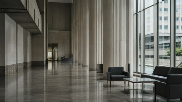 Vestíbulo moderno de edificio con columnas, suelo pulido y sillones negros junto