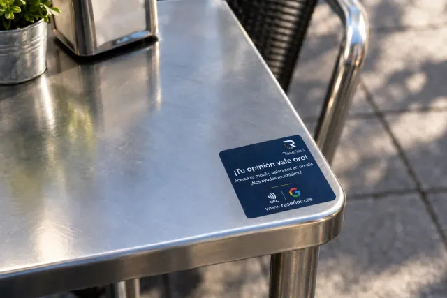 Etiqueta adhesiva sobre mesa metálica de terraza con texto en español