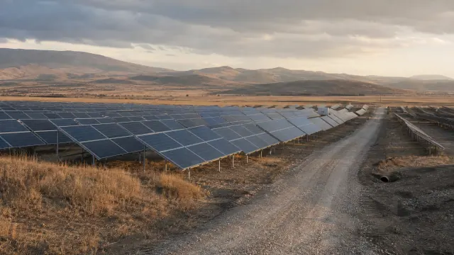 Huerto solar con paneles fotovoltaicos en terreno árido con montañas al fondo