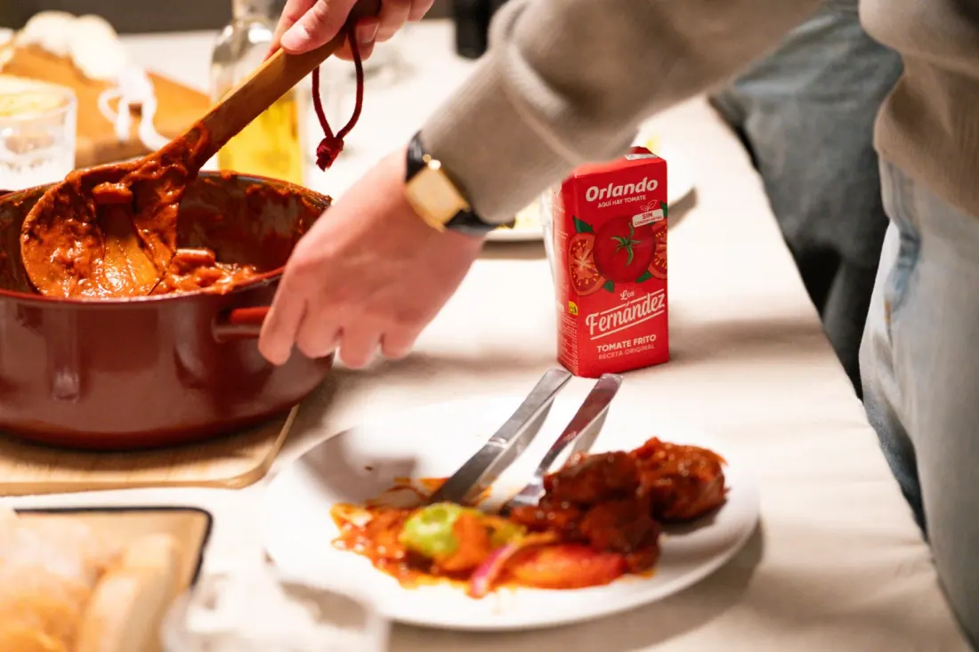 Una persona sirve un guiso de tomate junto a un envase de tomate frito Orlando