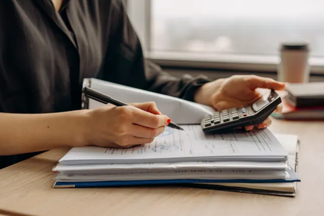 Una persona usa una calculadora sobre documentos en un escritorio