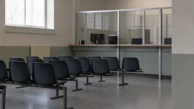 Varias sillas negras en una sala de espera con divisiones de vidrio y ventanas