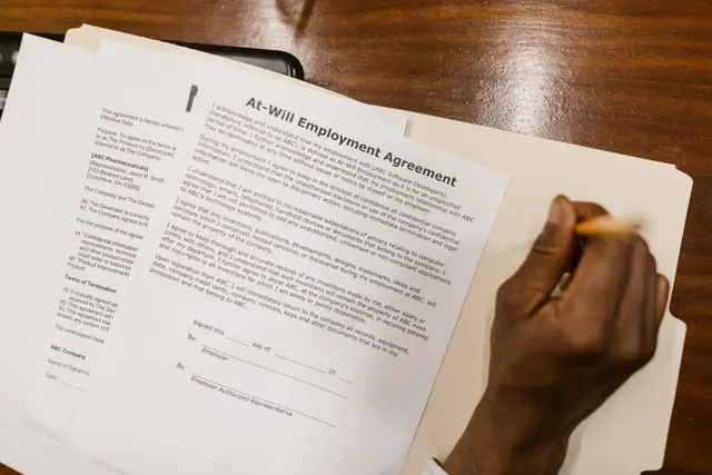 Dos personas firman un documento laboral sobre una mesa de oficina
