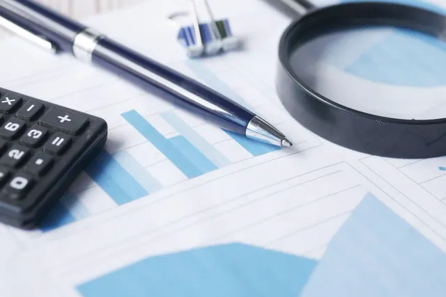 Gráficos financieros sobre una mesa junto a bolígrafo, calculadora y lupa