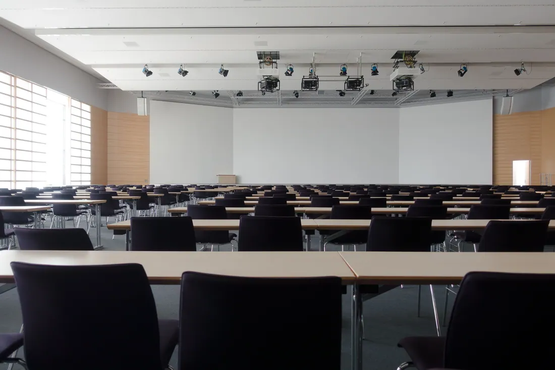 Sala de conferencias vacía con filas de mesas y sillas