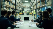 Grupo de trabajadores en reunión de oficina con vista a almacén logístico de fondo