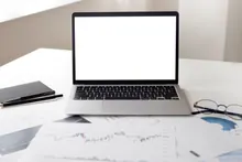 Portátil con pantalla en blanco sobre una mesa con gráficos financieros