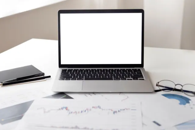 Portátil con pantalla en blanco sobre una mesa con gráficos financieros