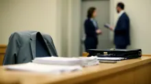 Una chaqueta y documentos sobre una mesa en un despacho con dos personas de fondo