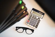 Una calculadora, unas gafas y varias carpetas sobre una mesa