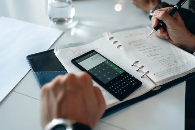 Manos usando una calculadora en el móvil junto a una agenda