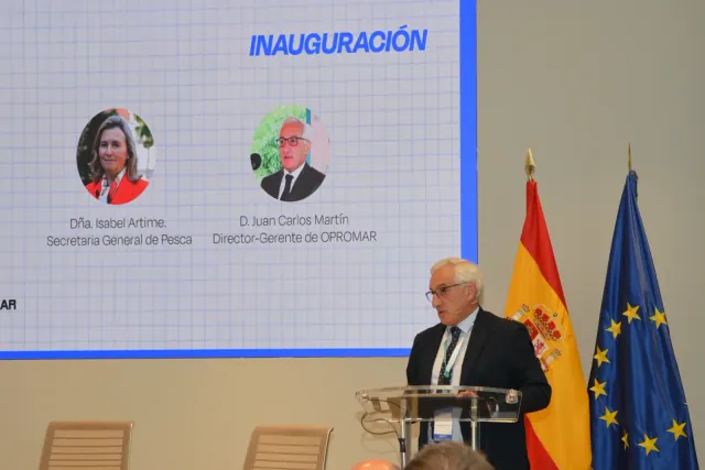 Un hombre habla en un atril junto a las banderas de España y la Unión Europea