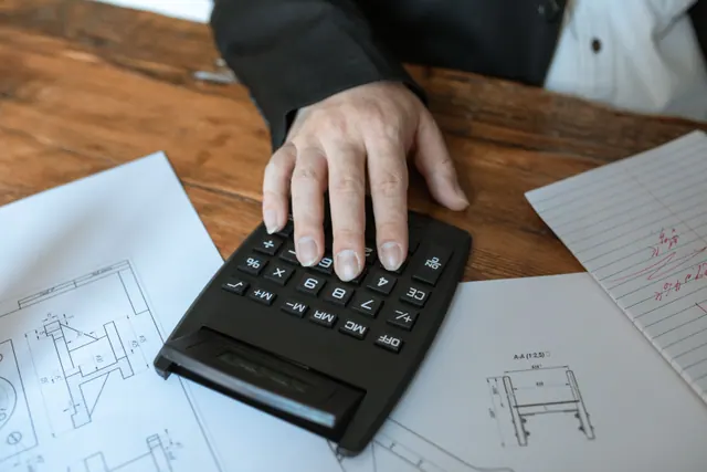 Una mano usando una calculadora sobre planos técnicos