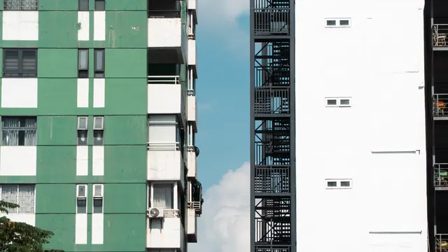 Fachada de edificio de viviendas con paneles verdes y blancos, junto a estructura metálica negra con escalera