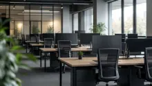 Espacio de oficina diáfano con mesas de madera, sillas negras y divisiones de cristal