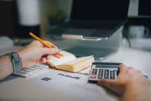 Manos usando una calculadora y un lápiz sobre un escritorio con gráficos