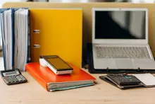 Escritorio de oficina con carpetas, calculadoras y un portátil abierto