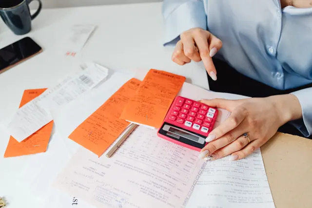 Una persona revisa recibos y factura con una calculadora en un escritorio